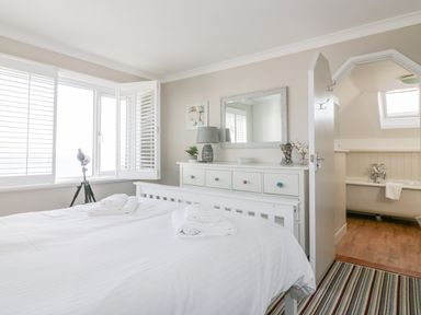 A bedroom with a white bed and dresser next to a door leading to a bathroom at Bayview in Mevagissey