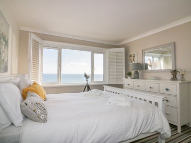 A bedroom with a large bed facing a window with a sea view a dresser with a mirror and a lamp Bayview Mevagissey