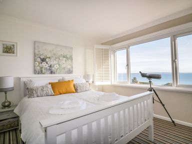A bedroom with a white bed near a window with a telescope and ocean view at Bayview in Mevagissey