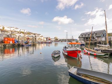 A harbor with boats in the water buildings on the hillside and a large building by the water at Bayview in Mevagissey
