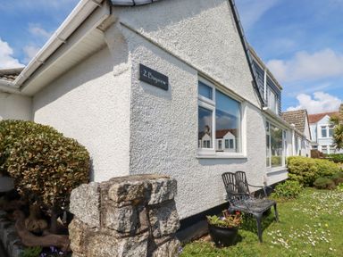 The exterior of a white house with a sign reading 2 Bayview with a small garden and metal bench at Bayview Mevagissey