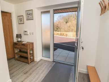 An entryway with an open door showing an outdoor area a wooden console table with a lamp and two pictures on the wall at High Tide House in Craster