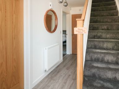 A hallway with wooden doors a grey carpeted staircase a round mirror and a radiator at High Tide House in Craster