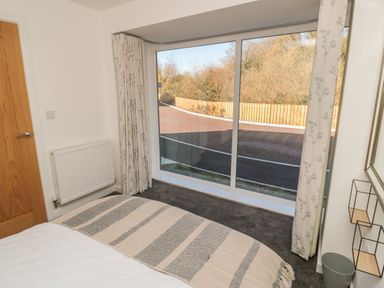 A bedroom with a bed near a large window with curtains and a view of a road and fence at High Tide House in Craster