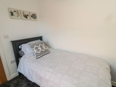 A single bed with patterned bedding and a decorative cushion against a white wall with three fish artwork at High Tide House in Craster