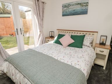 A bedroom with a double bed green and pink pillows and a patterned blanket two bedside tables and glass doors opening to a garden at High Tide House in Craster