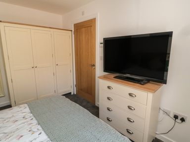 A bedroom with a bed, a wardrobe, a wooden door, a chest of drawers with a television on top at High Tide House in Craster