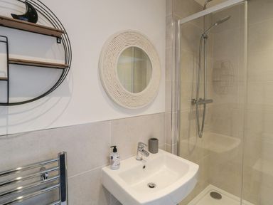 A bathroom with a white sink a round mirror a glass shower enclosure and a towel rail at High Tide House in Craster