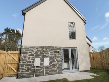 The exterior side of a house with a stone lower wall a beige upper wall a single window glass doors and a wooden fence at High Tide House in Craster