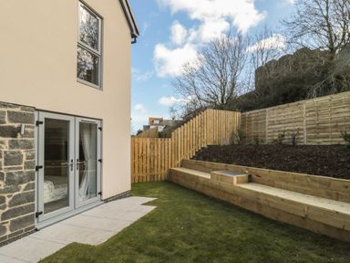 A backyard with grass lawn stone and glass double doors a wooden fence and tiered wooden planter boxes at High Tide House in Craster
