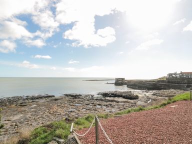 A rocky coastline with a stone jetty and buildings in the distance at High Tide House in Craster