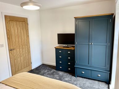 A bedroom corner with a wooden door a blue wardrobe and chest of drawers with a television on top at High Tide House in Craster