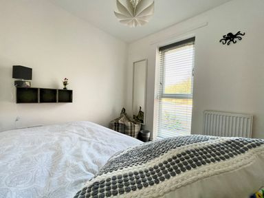 A bedroom with a bed, wall-mounted shelves, window with blinds, mirror, bean bag, and radiator at High Tide House in Craster