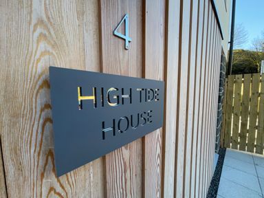 A wooden exterior wall with a metal sign reading High Tide House and the number 4 near a wooden gate at High Tide House in Craster