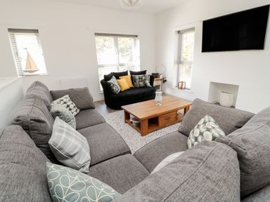 A living room with gray sofas a wooden coffee table a black armchair and a wall mounted television at High Tide House in Craster
