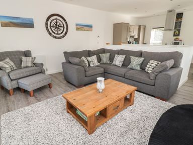 A living room with a gray sofa and armchair a wooden coffee table and a white rug at High Tide House in Craster