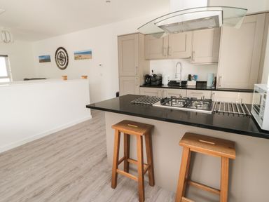 A kitchen with two wooden stools at a black countertop and beige cabinets at High Tide House in Craster