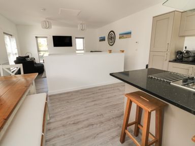 A kitchen with wooden stools and a dining table with benches next to a living area with a wall-mounted TV at High Tide House in Craster