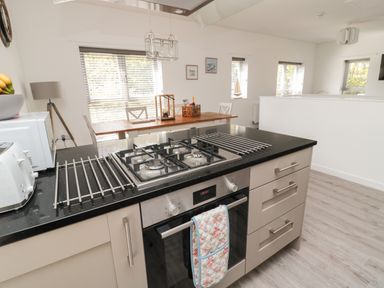A kitchen island with a gas stove oven and drawers with a dining table and chairs in the background at High Tide House in Craster