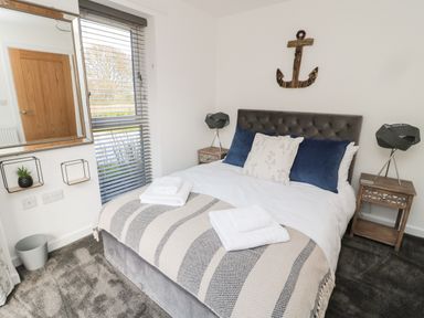 A bedroom with a bed with pillows and folded towels bedside tables with lamps a mirror and window blinds at High Tide House in Craster