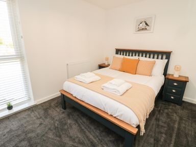 A bedroom with a bed with folded towels bedside tables and a window with blinds at High Tide House in Craster