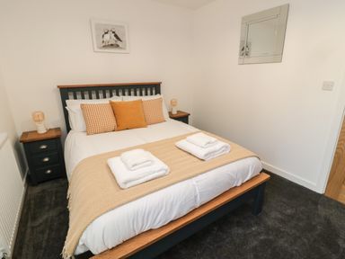 A bedroom with a bed with three pillows two bedside tables with lamps a wall mirror and a puffin picture at High Tide House in Craster