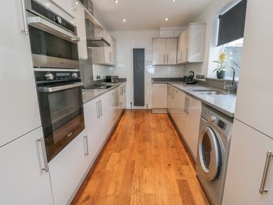 A galley kitchen with wooden floor appliances and cabinets at Beach Cove View in Newbiggin-by-the-Sea