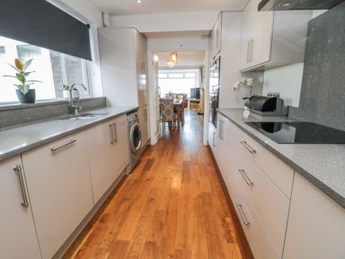 A kitchen with wooden floor cabinets countertops a washing machine and a dining area visible at Beach Cove View in Newbiggin-by-the-Sea