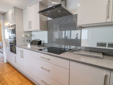 A kitchen with grey countertops white cabinets an electric stovetop a stainless steel oven and a wooden floor at Beach Cove View in Newbiggin-by-the-Sea