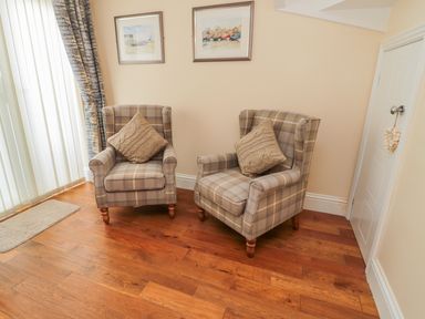 Two plaid armchairs with cushions in a corner near a door with wall art at Beach Cove View in Newbiggin-by-the-Sea