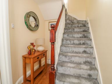 A carpeted staircase with wooden handrail next to a wooden console table with a lamp and decorative item at Beach Cove View in Newbiggin-by-the-Sea