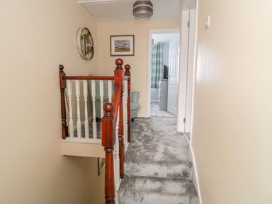 A carpeted staircase landing with wooden banisters leading to a hallway with an armchair and a room with a television at Beach Cove View in Newbiggin-by-the-Sea