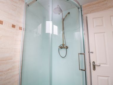 A glass-enclosed shower with a brass showerhead and beige tiled walls at Beach Cove View in Newbiggin-by-the-Sea