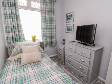 A small bedroom with a single bed next to a window and a gray dresser with a television on top at Beach Cove View in Newbiggin-by-the-Sea