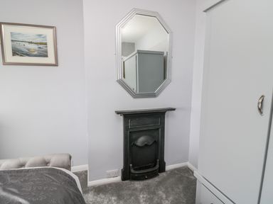 A bedroom corner with a bed edge visible a framed painting on the wall a small black fireplace and a mirror above it at Beach Cove View in Newbiggin-by-the-Sea