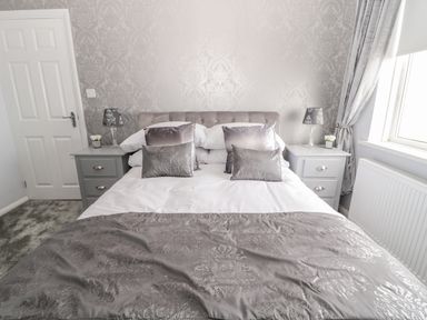 A bedroom with a double bed flanked by two bedside tables with lamps and decor at Beach Cove View in Newbiggin-by-the-Sea