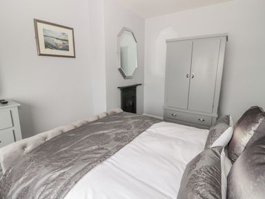 A bedroom with a bed a gray wardrobe a chest of drawers a mirror and a framed picture on the wall at Beach Cove View in Newbiggin-by-the-Sea