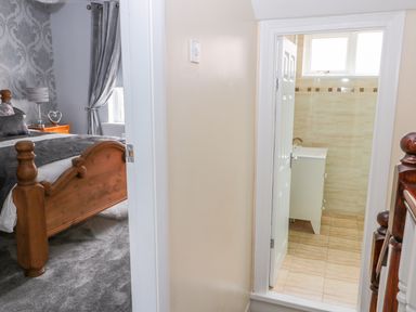 View of a bedroom with a wooden bed and grey curtains next to a bathroom with tiled walls at Beach Cove View in Newbiggin-by-the-Sea
