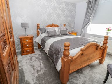 A bedroom with a wooden bed and matching bedside tables with lamps at Beach Cove View in Newbiggin-by-the-Sea