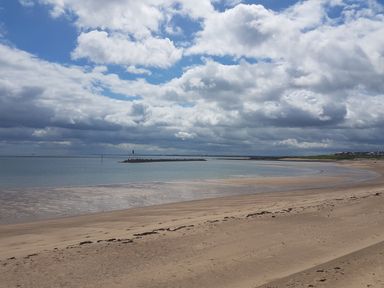 A sandy beach with a curved shoreline and a rocky breakwater in the water under a cloudy sky at Beach Cove View in Newbiggin-by-the-Sea