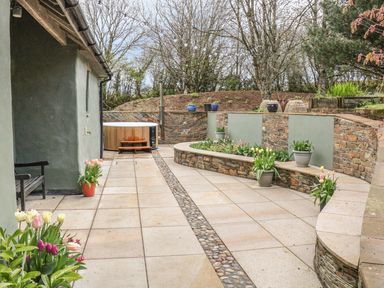 An outdoor patio area with a hot tub and potted plants along stone walls at Spring Park Farmhouse in Launceston