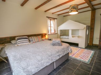 A bedroom with a large bed and a small house-shaped bed frame near a window on a tiled floor at Woodcutters in Rezare near Launceston