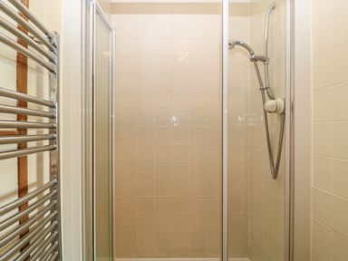 A shower enclosure with tiled walls a sliding glass door and a mounted showerhead with a temperature control and a chrome towel radiator in a bathroom at Woodcutters Rezare near Launceston