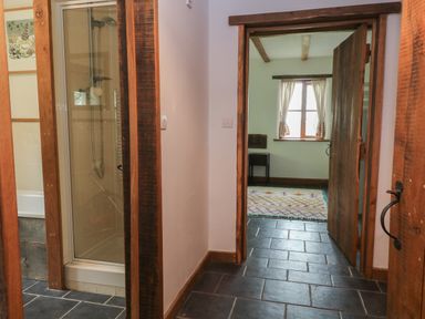A hallway with tiled floor leading to a room with a window and curtains and a wooden door and a shower cubicle to the side at Woodcutters Rezare near Launceston