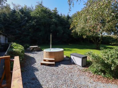 An outdoor area with a wooden hot tub steps a picnic table a storage box gravel ground and trees at Woodcutters in Rezare near Launceston