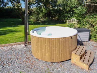 An outdoor wooden hot tub with steps on a gravel area near a garden bench at Woodcutters Rezare near Launceston