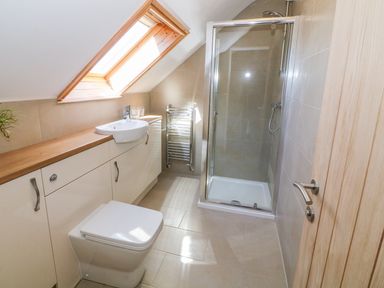 A bathroom with a shower, toilet, sink, wooden countertop, and skylight window at Llain Haf in Llangefni