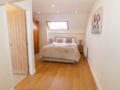 A bedroom with a bed two bedside tables lamps a wooden wardrobe skylight window and wooden door at Llain Haf in Llangefni