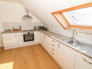 A kitchen with white cabinets a stainless steel oven countertop appliances and a large angled window at Llain Haf in Llangefni