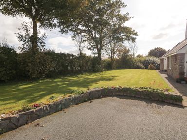 A garden with trees grass and a stone wall next to a stone house at Llain Haf in Llangefni